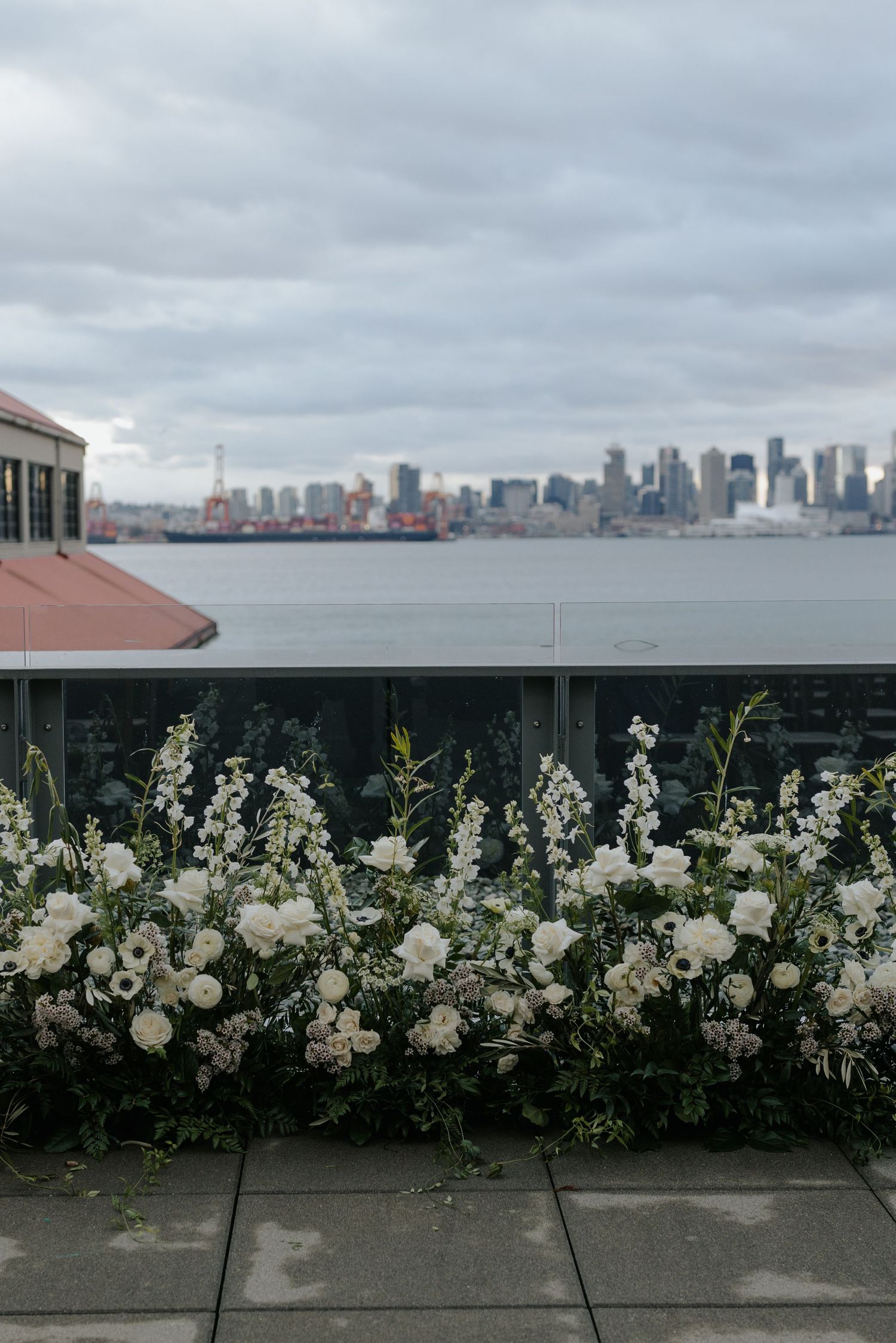 White floral arrangements line a concrete wall with city skyline views in the background.