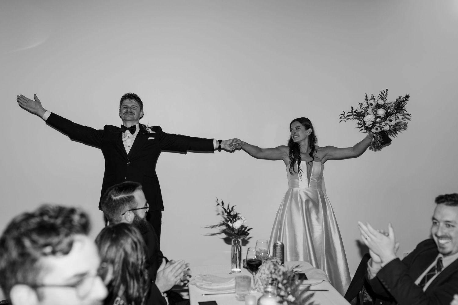 A celebratory moment at a wedding reception as a couple raises their arms in joyful triumph.