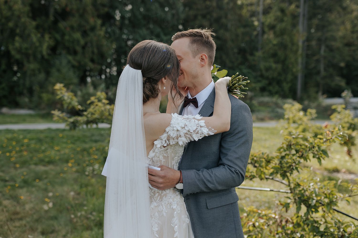 A romantic couple in wedding attire embraces in a lush garden setting during their outdoor ceremony.