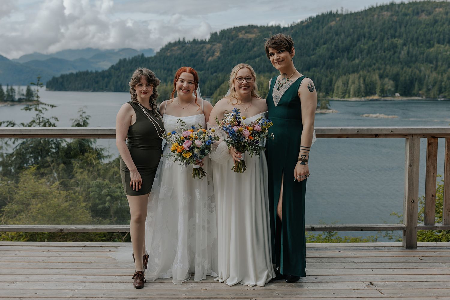 Wedding group gathers on wooden deck with stunning Pacific Northwest landscape in background.