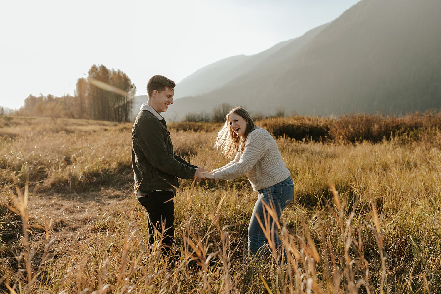 A couple shares tender moments in a golden field with mountains in the distance.