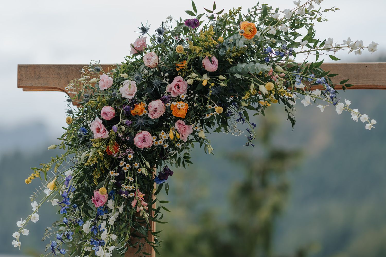 Elegant floral arch with pink and orange blooms decorates a rustic outdoor wedding venue.