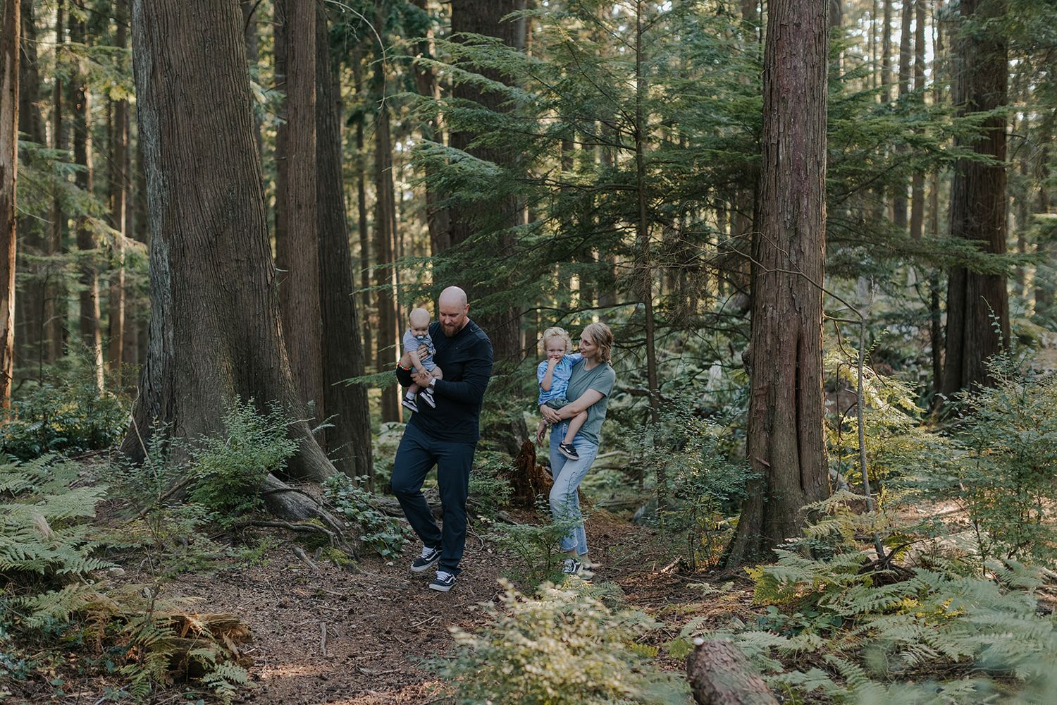 Two people hiking together on a forest trail surrounded by tall evergreen trees.