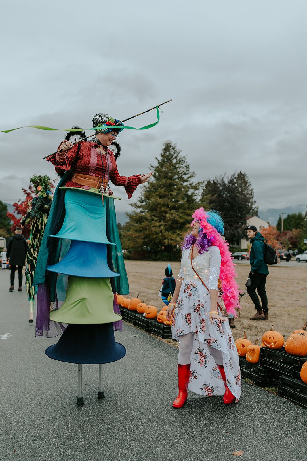 Colorful costumed performers in bell-shaped outfits at an outdoor event.