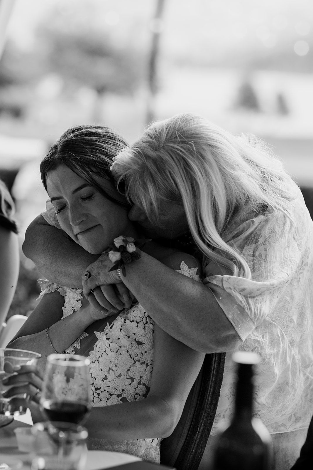Black and white photo of wedding guests laughing and embracing during an emotional reception moment.