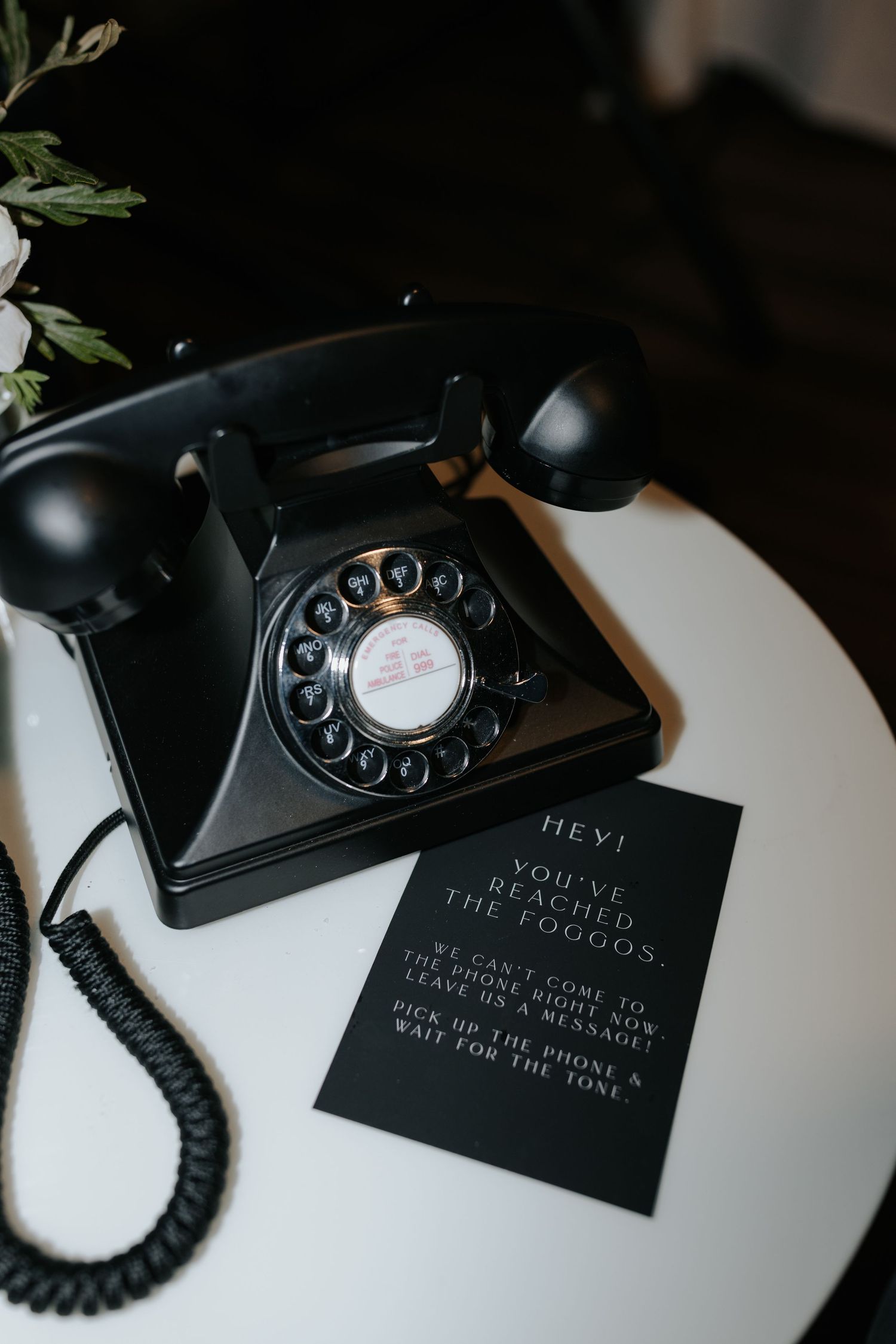 Vintage black rotary telephone with black business cards displayed on white surface.