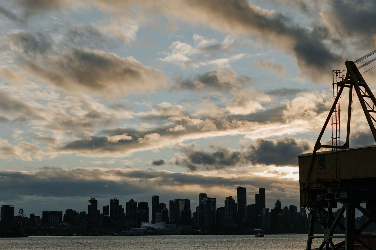 Dramatic cloudy sunset sky over a city skyline with silhouetted buildings and cranes.