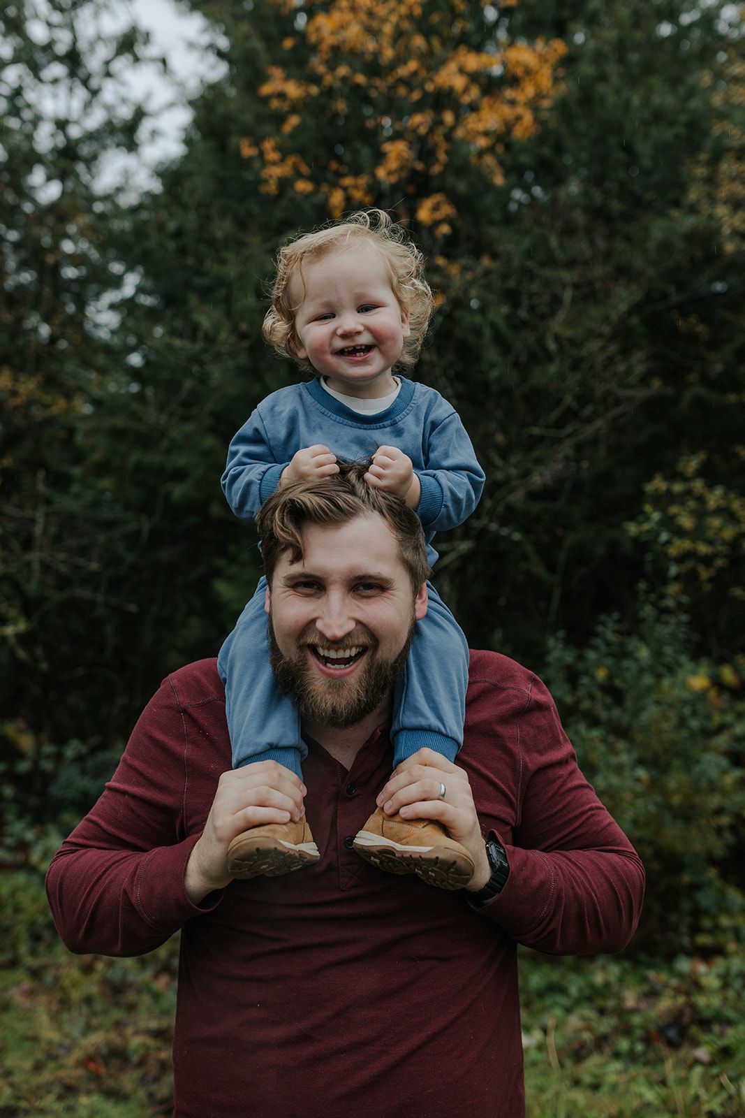 A toddler sits happily on shoulders during an outdoor autumn photoshoot.