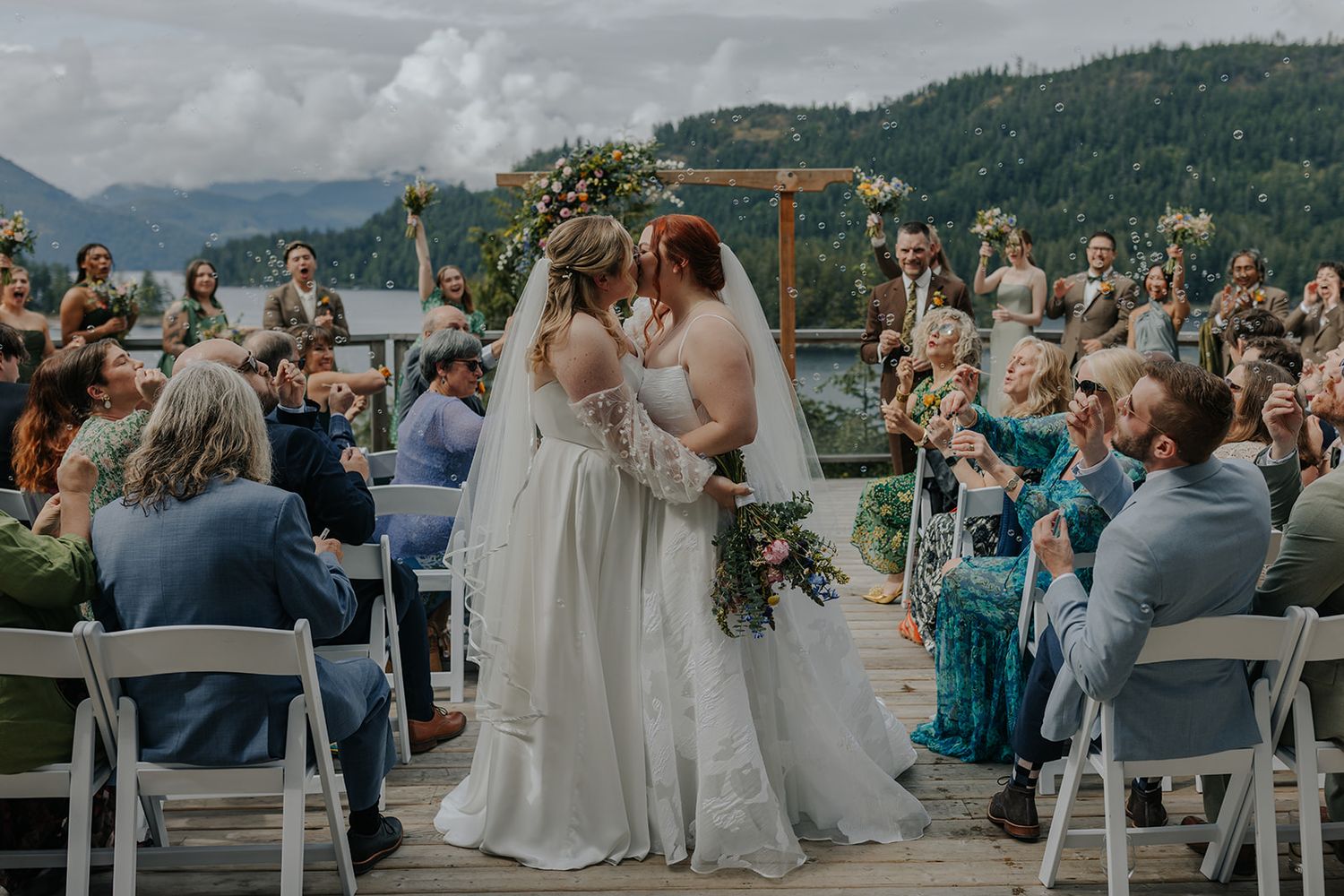 Wedding guests seated on wooden deck watching ceremony with mountain views.