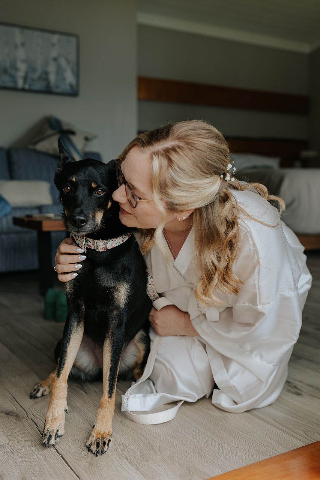 Person in white robe sharing tender moments with black dog on light wooden floor.