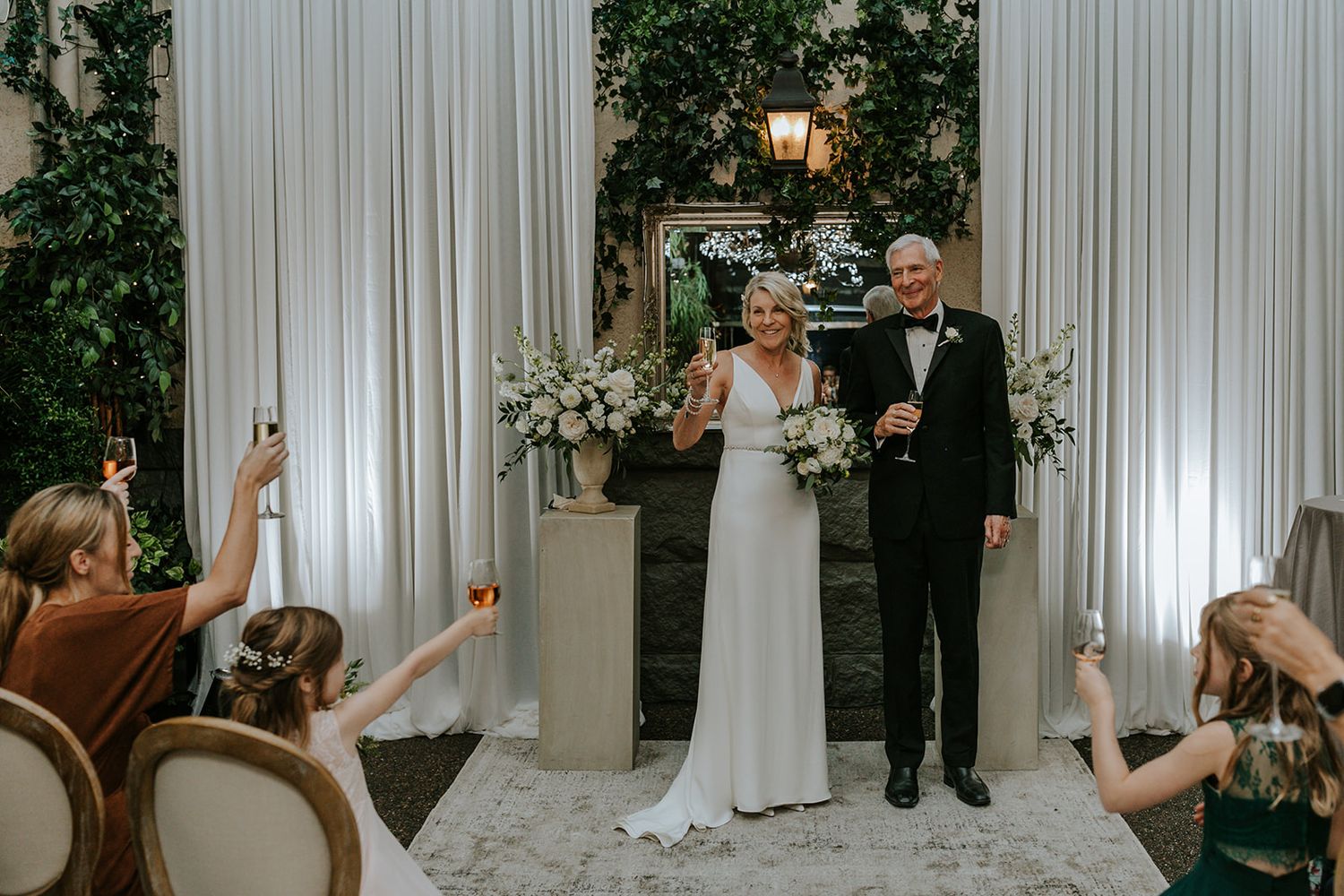 Indoor wedding ceremony setup with white drapes and floral decorations.
