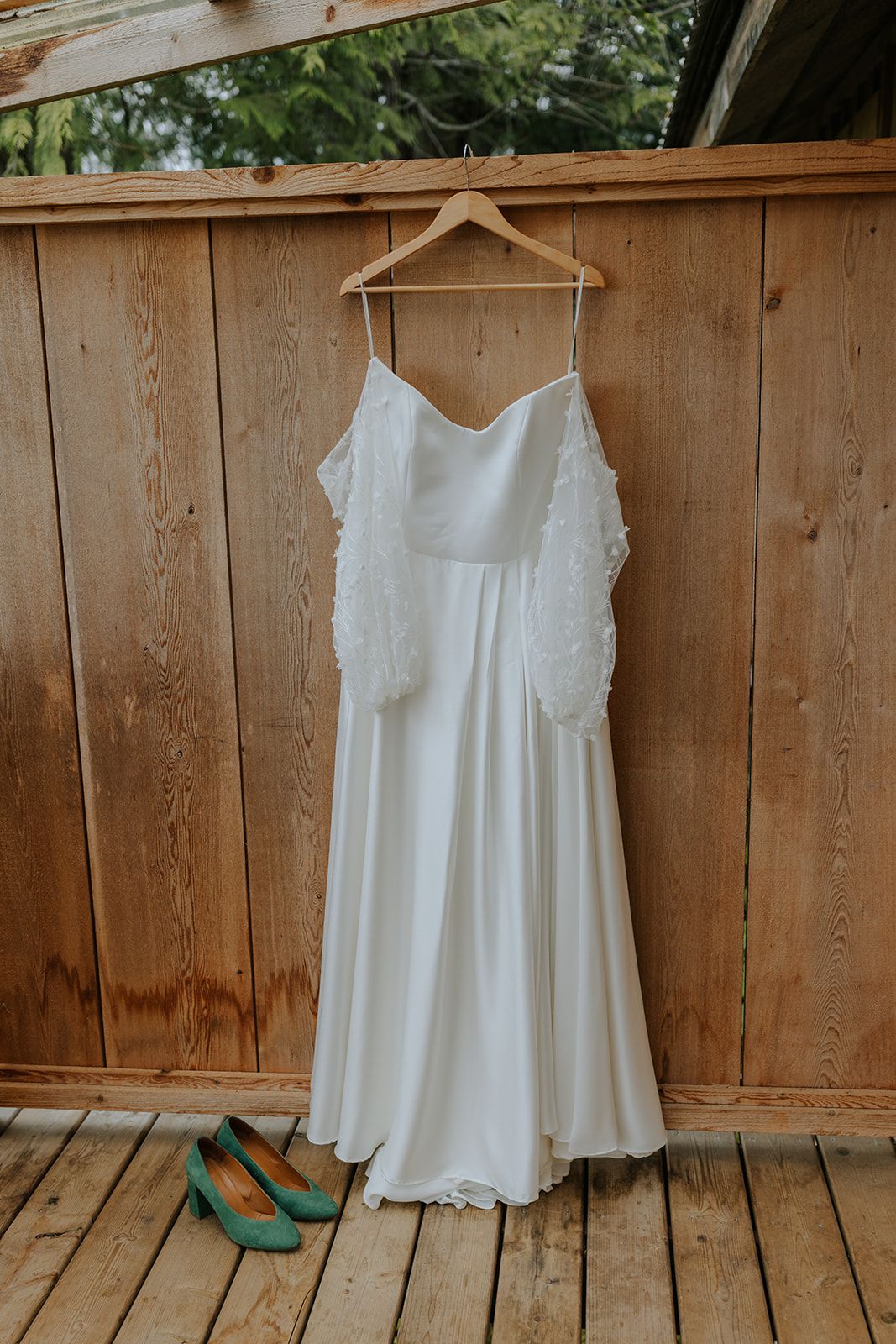 White wedding dresses and teal shoes displayed against rustic wooden fence backdrop.