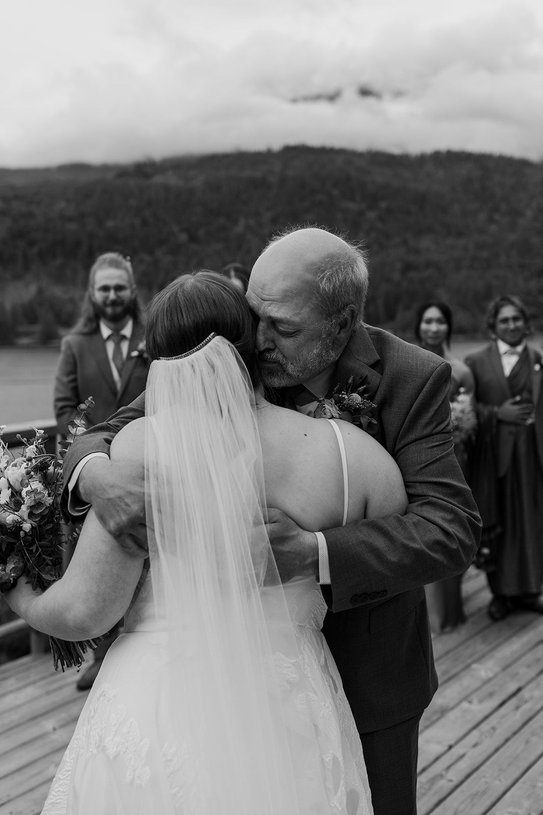 Emotional wedding ceremony moment on a scenic deck overlooking mountains and water.