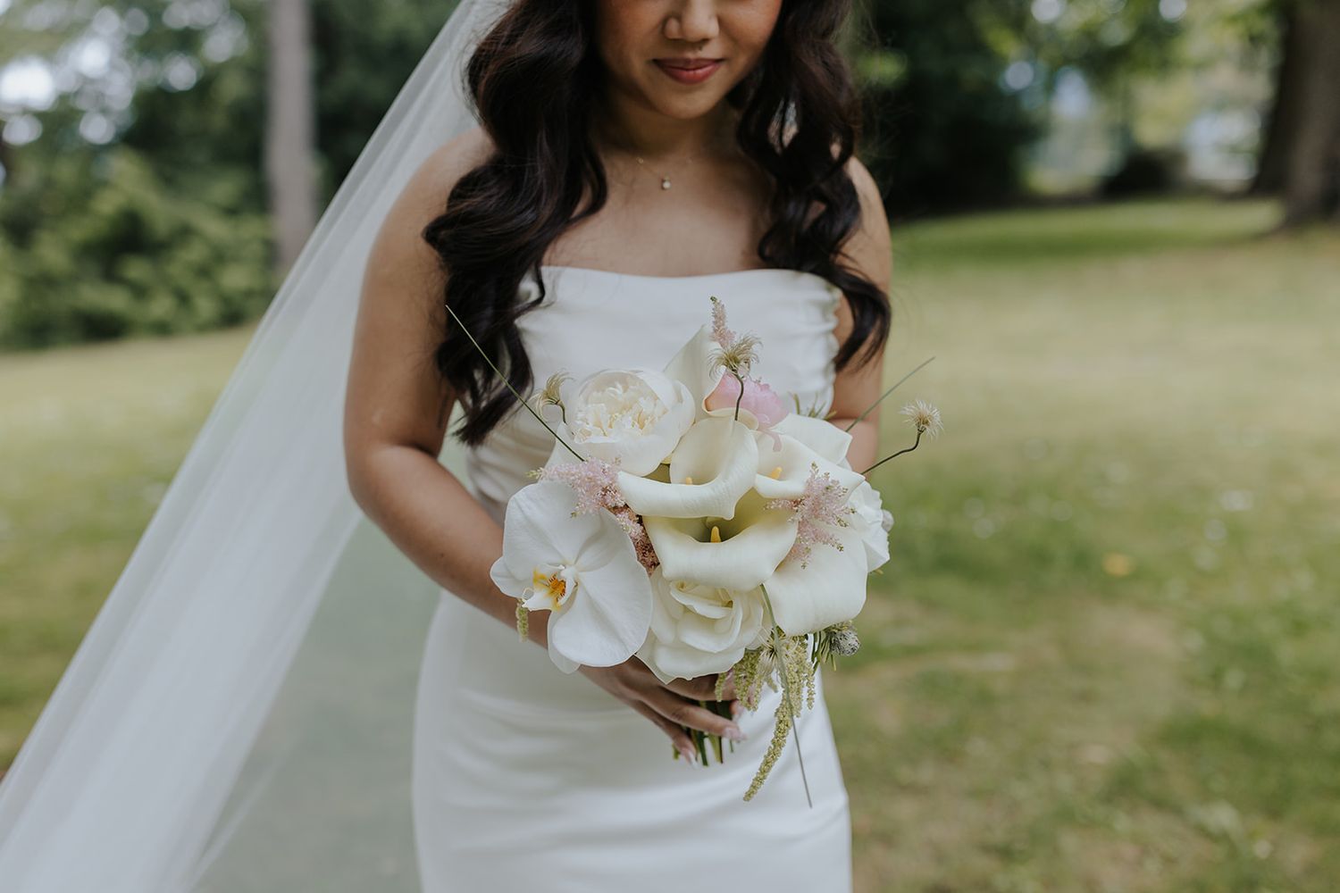 Elegant bridal bouquet of white orchids against a sunny outdoor background.