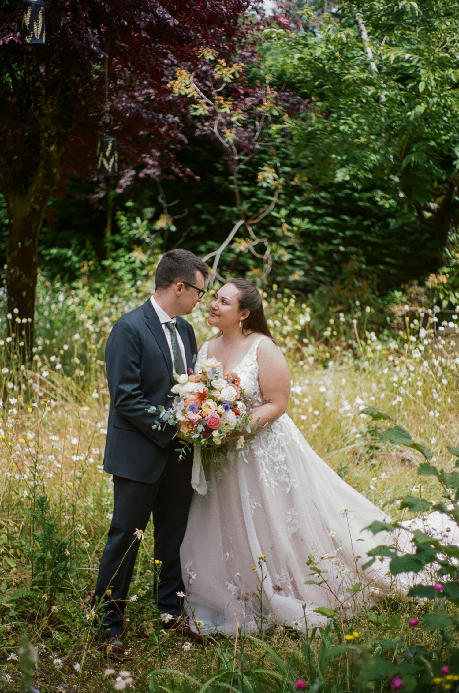 A romantic wedding couple shares intimate moments in a lush garden setting with wildflowers and greenery.