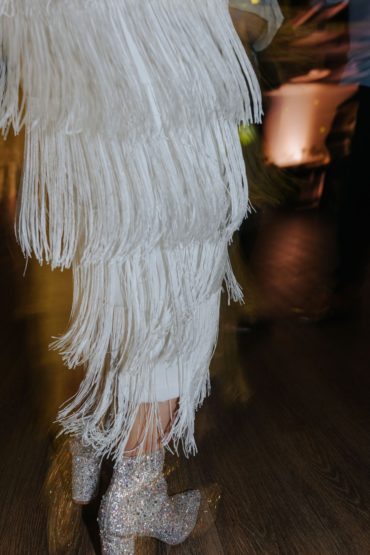 Close-up of white fringe details and sparkly boots on a wedding dress.