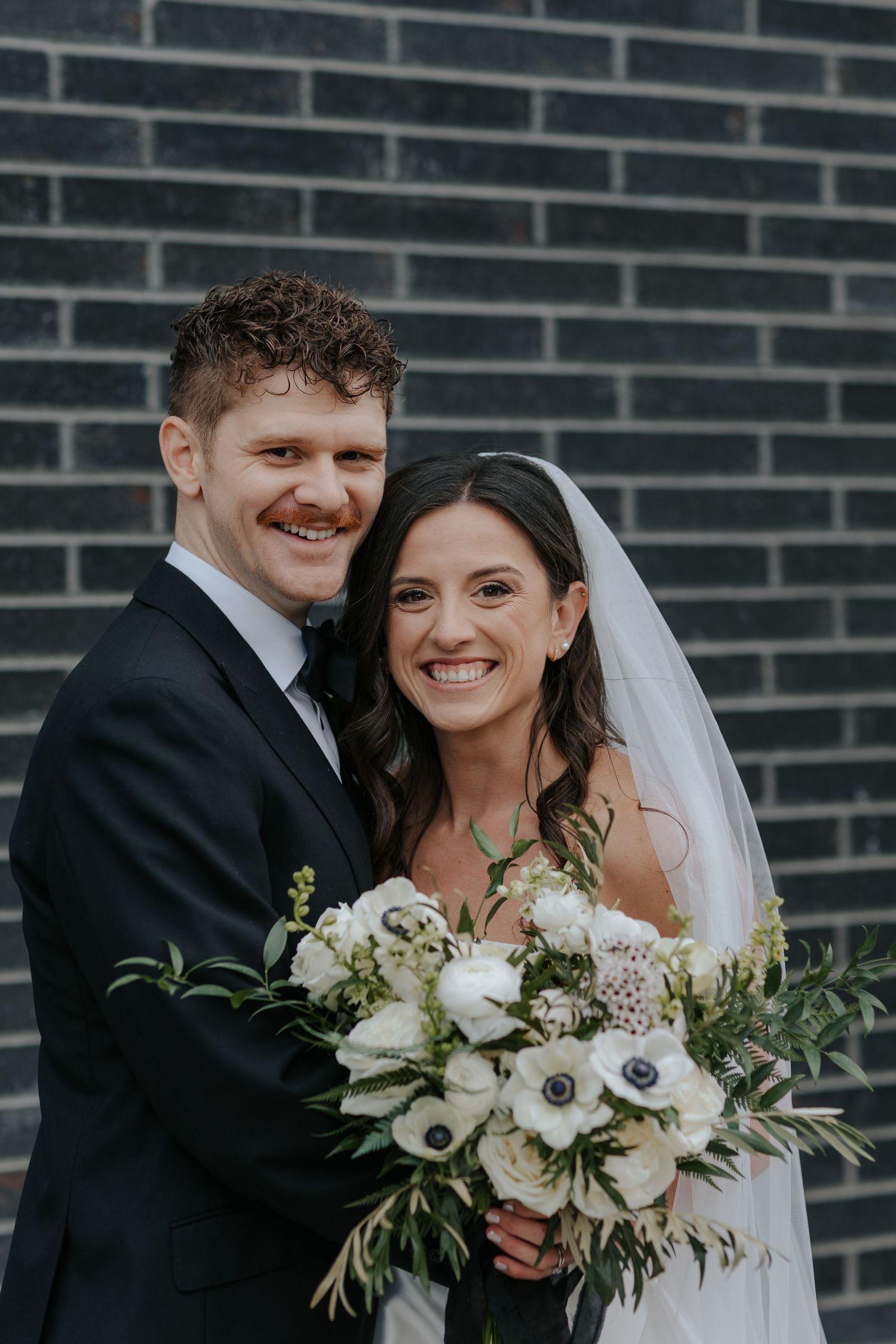 Wedding portrait against dark brick wall with elegant white floral bouquet.