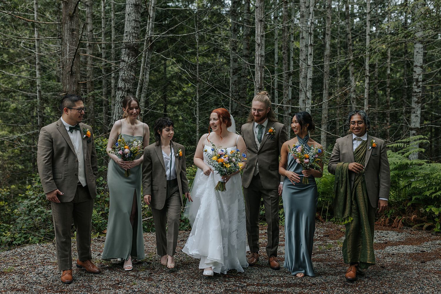 Wedding group photo session in a wooded area with evergreen trees and natural lighting.