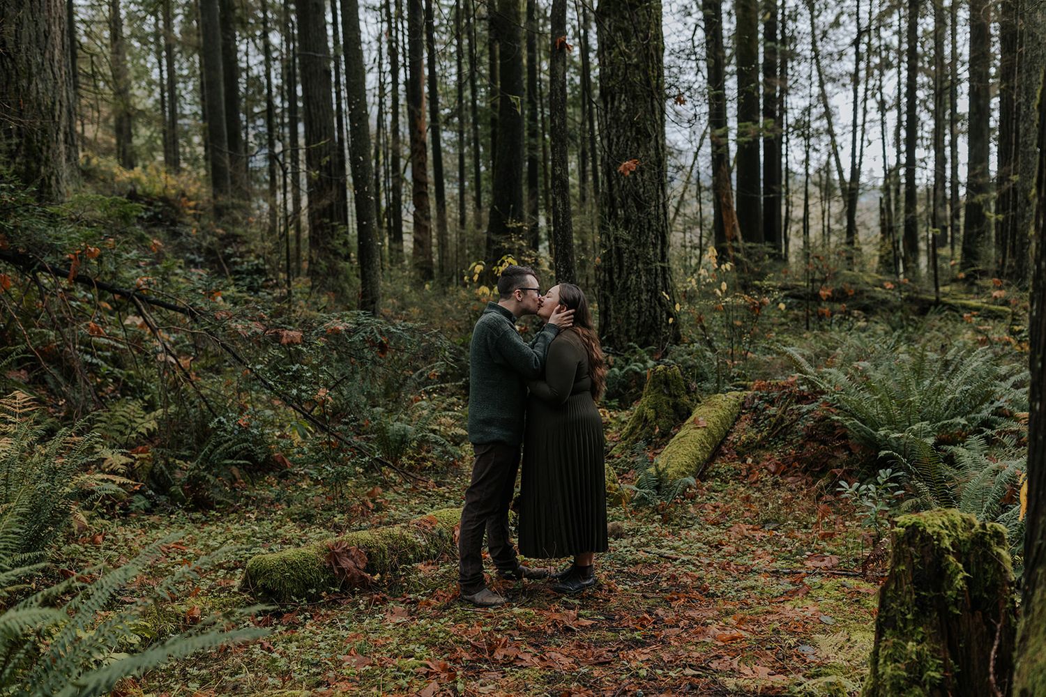 A couple embracing on a misty forest path surrounded by tall evergreen trees.