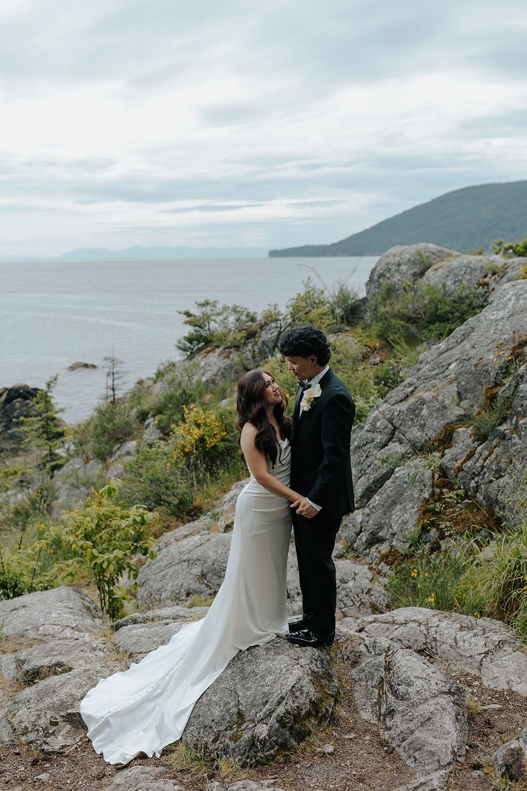 Wedding couple poses on rocky coastal cliffs with dramatic ocean views in the background.