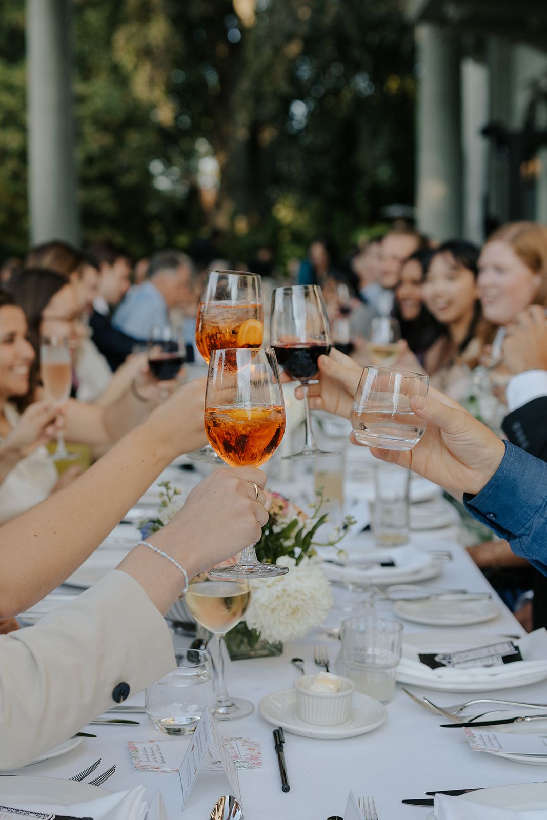 Wedding guests raise wine glasses in a toast at an elegant outdoor reception.