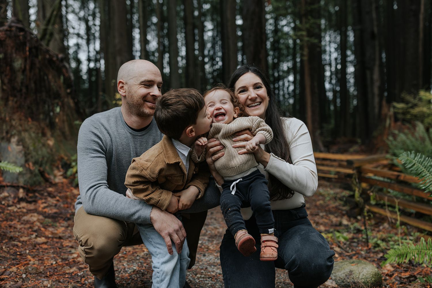 A family shares joyful moments together while sitting on fallen logs in a moody forest setting.