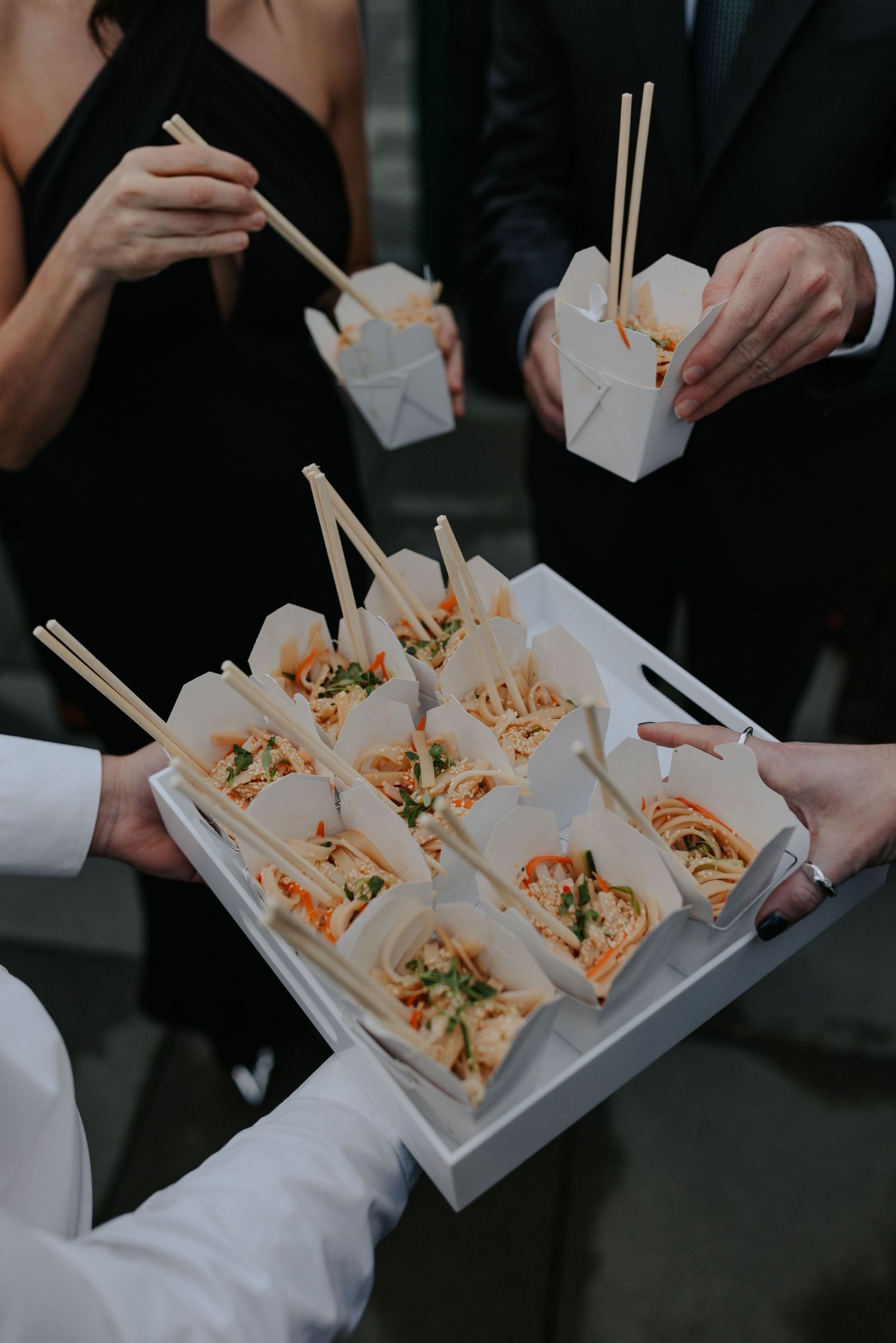 Wedding guests serve themselves from a tray of Chinese takeout boxes at an elegant reception.
