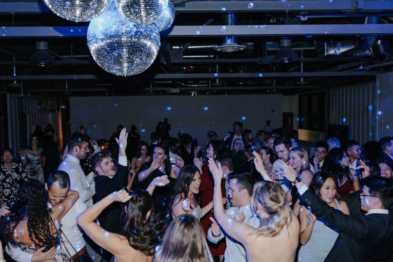 Wedding reception dance floor filled with guests dancing under disco balls.