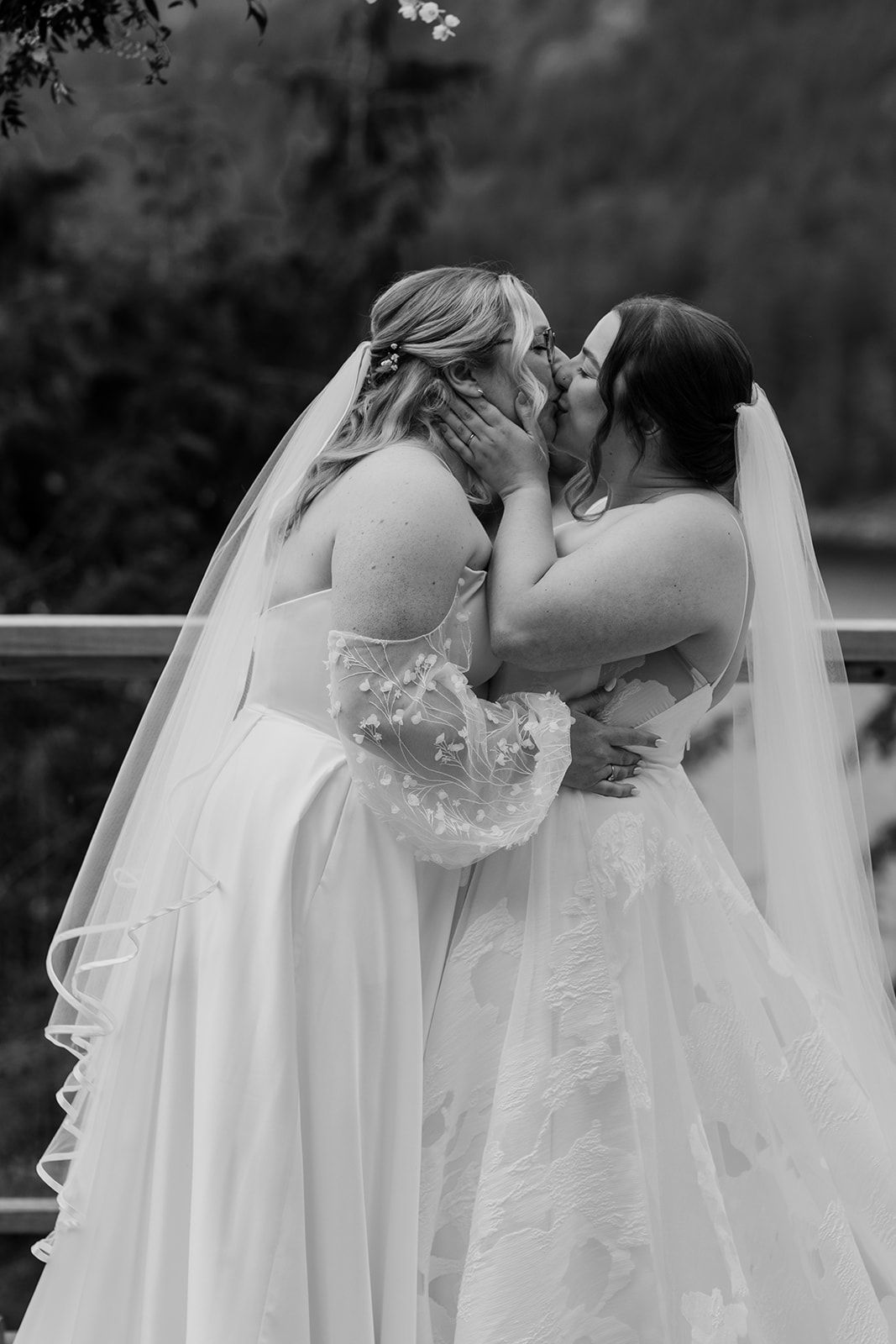 Black and white photo of two brides in white dresses sharing a tender moment during their ceremony.