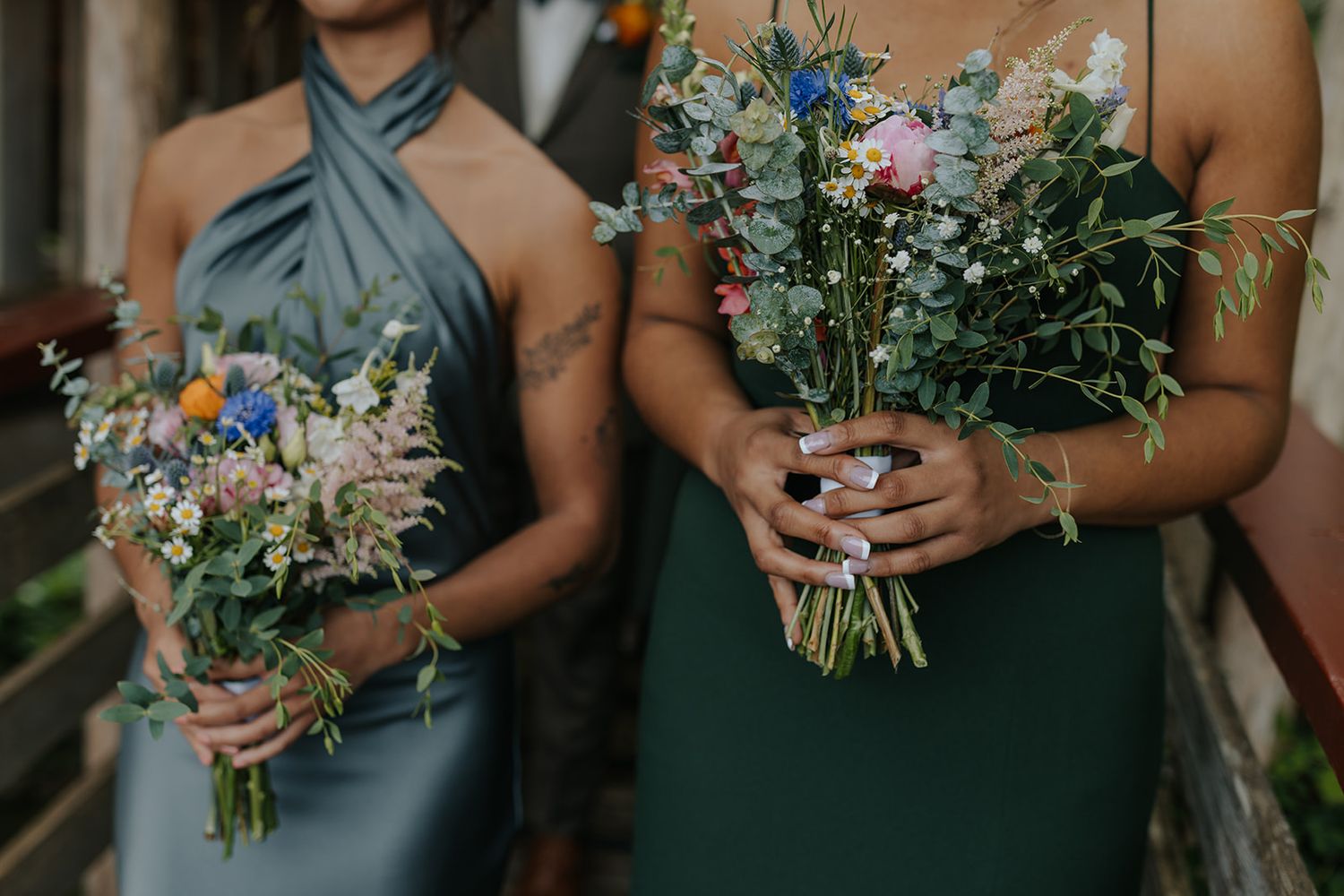 Close-up of wedding bouquets with wildflowers held by attendants in green and blue dresses.