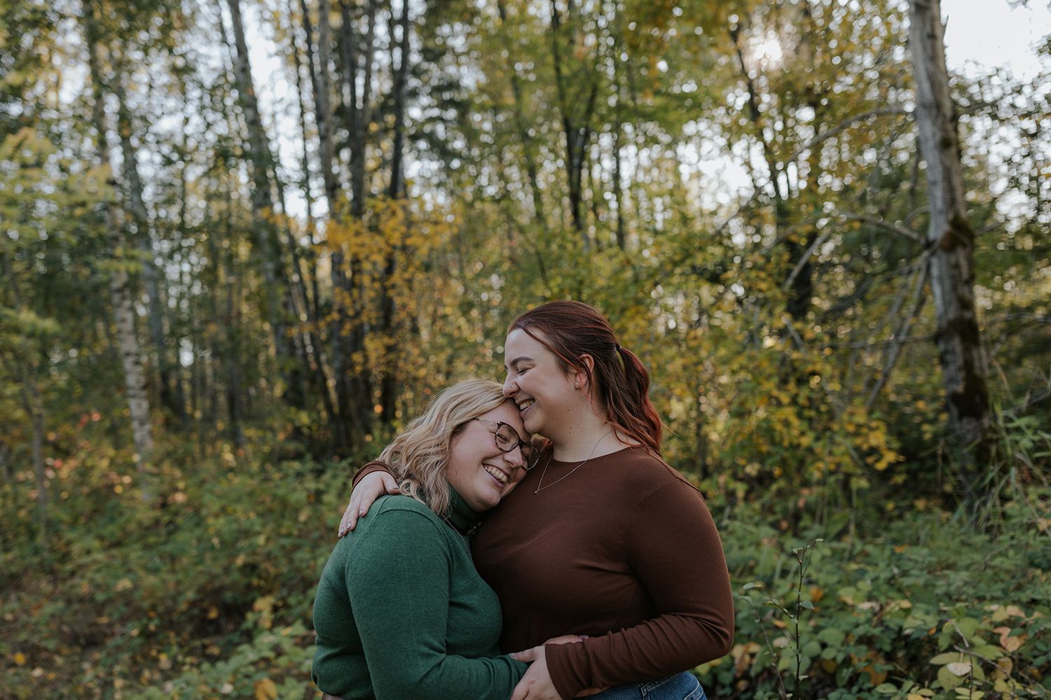 A couple sharing an intimate embrace while surrounded by autumn trees and foliage.
