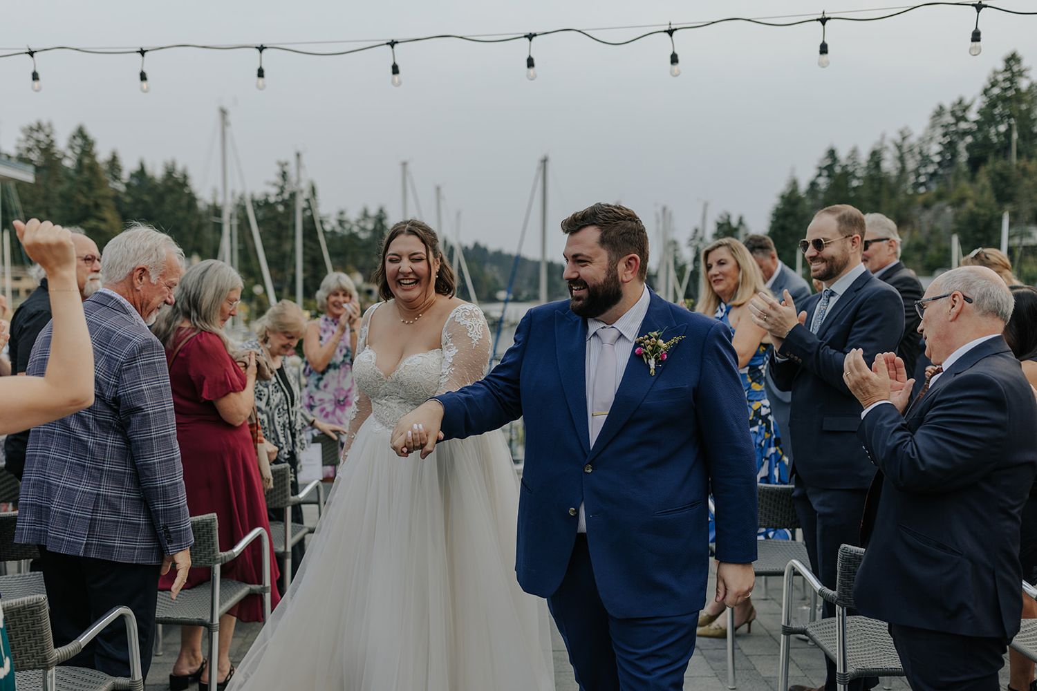 Outdoor wedding reception with string lights and guests celebrating near a marina.