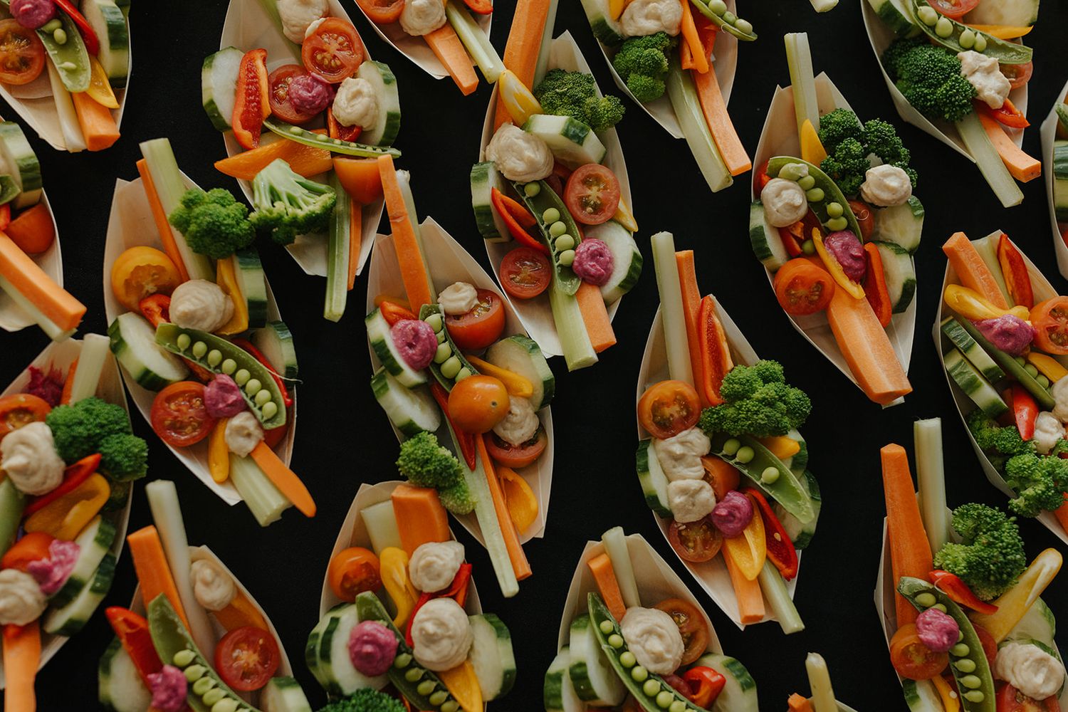 Overhead view of colorful appetizer platters arranged in rows featuring vegetables and dips.