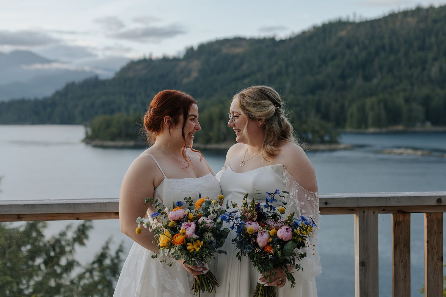 Wedding couple embracing on deck with scenic mountain lake vista.