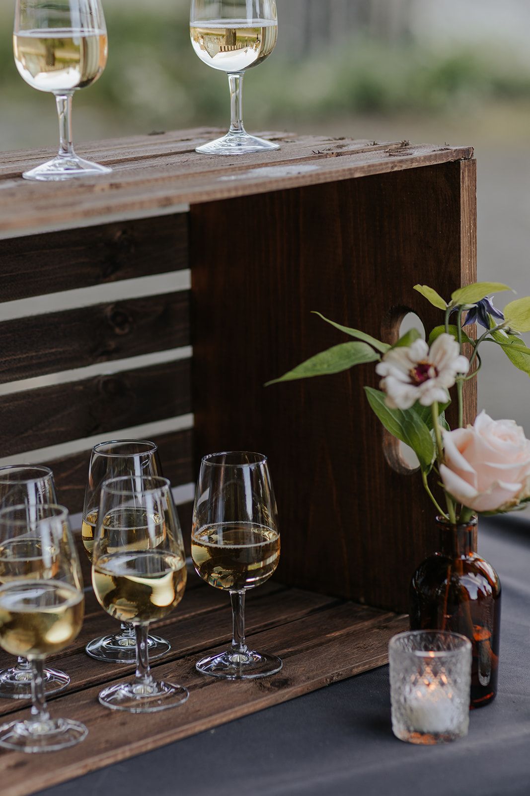 Wine glasses and floral arrangements line a wooden shelf at an elegant event.