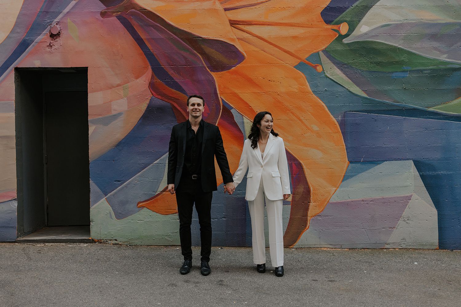 A couple poses in front of a vibrant colorful mural with geometric patterns.