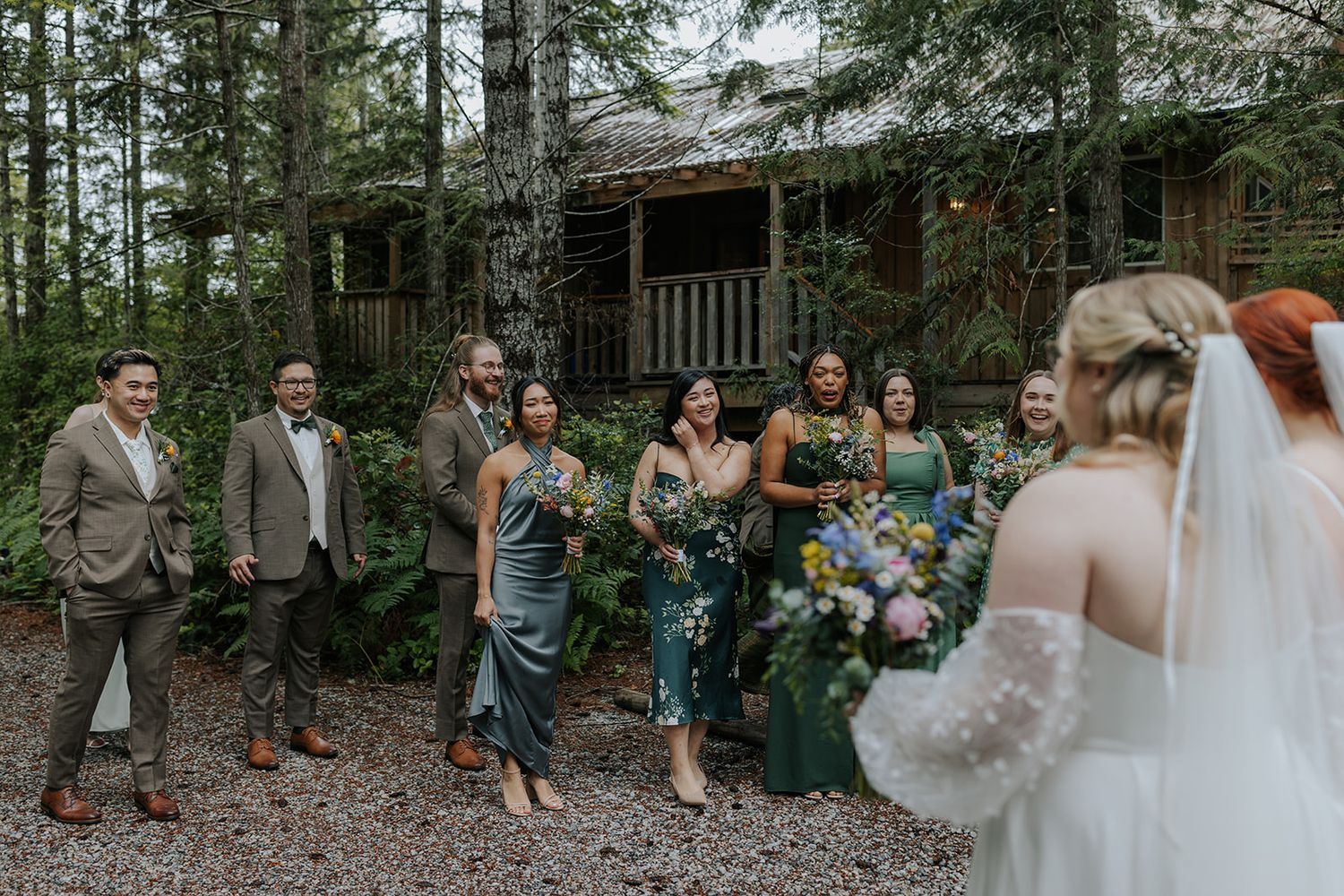 Wedding celebration group poses together on wooded path surrounded by evergreen trees.