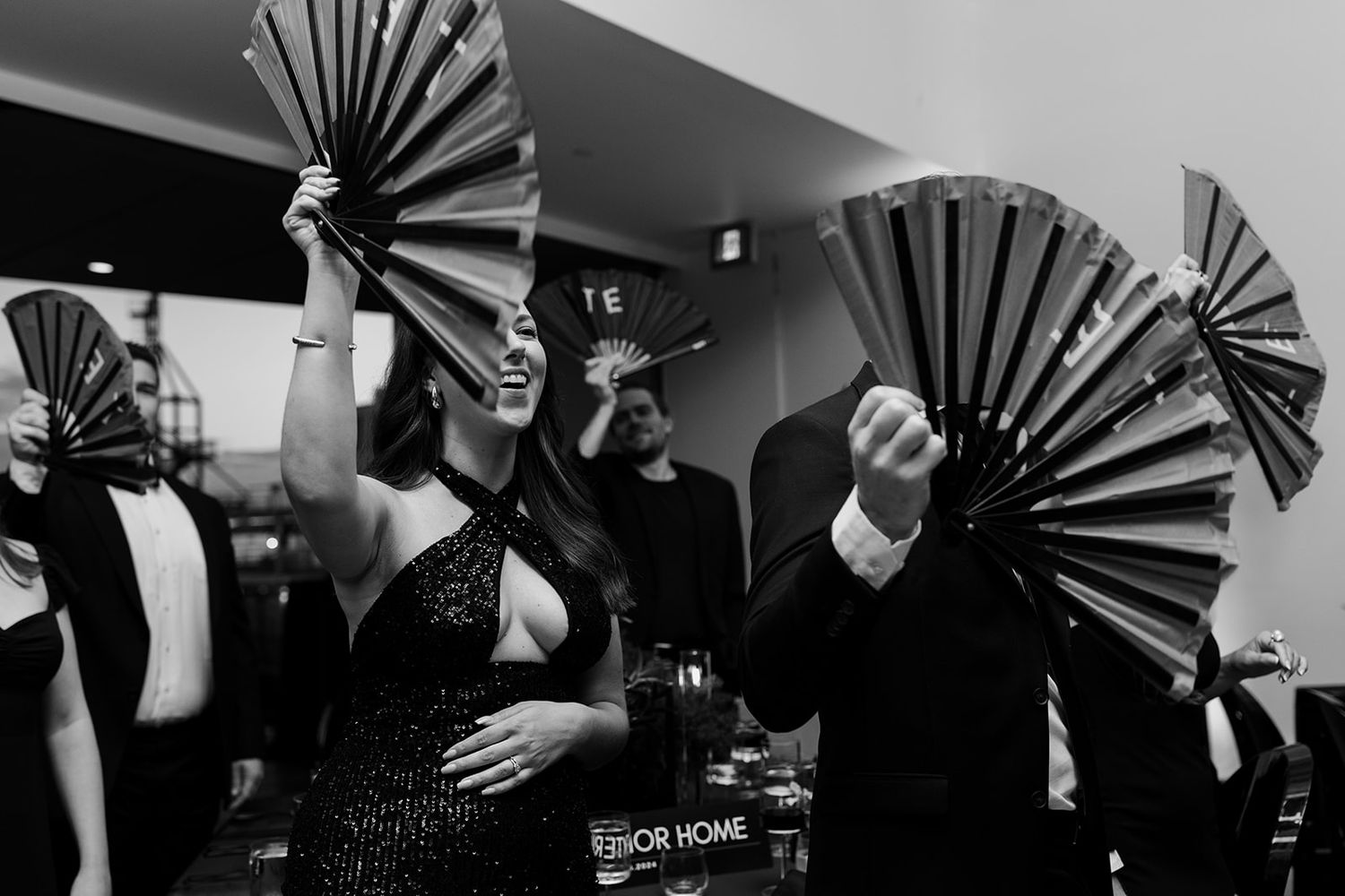 Artistic black and white photo of wedding guests holding decorative hand fans.