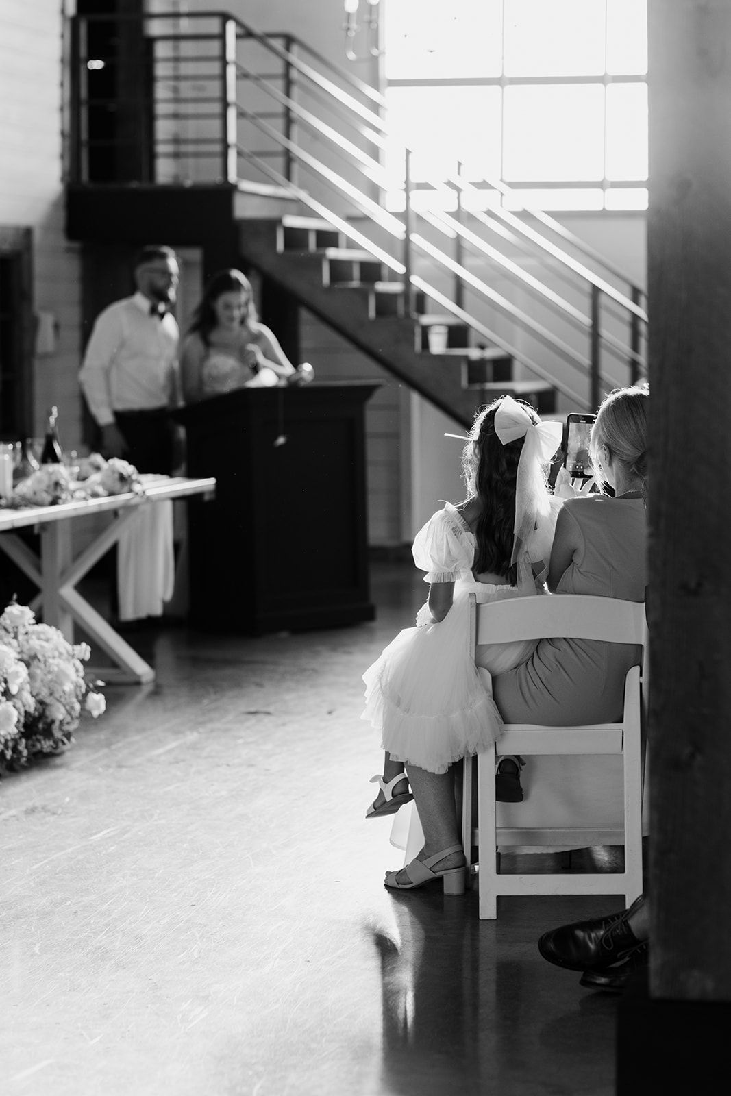 Wedding guests seated in white chairs during indoor ceremony.
