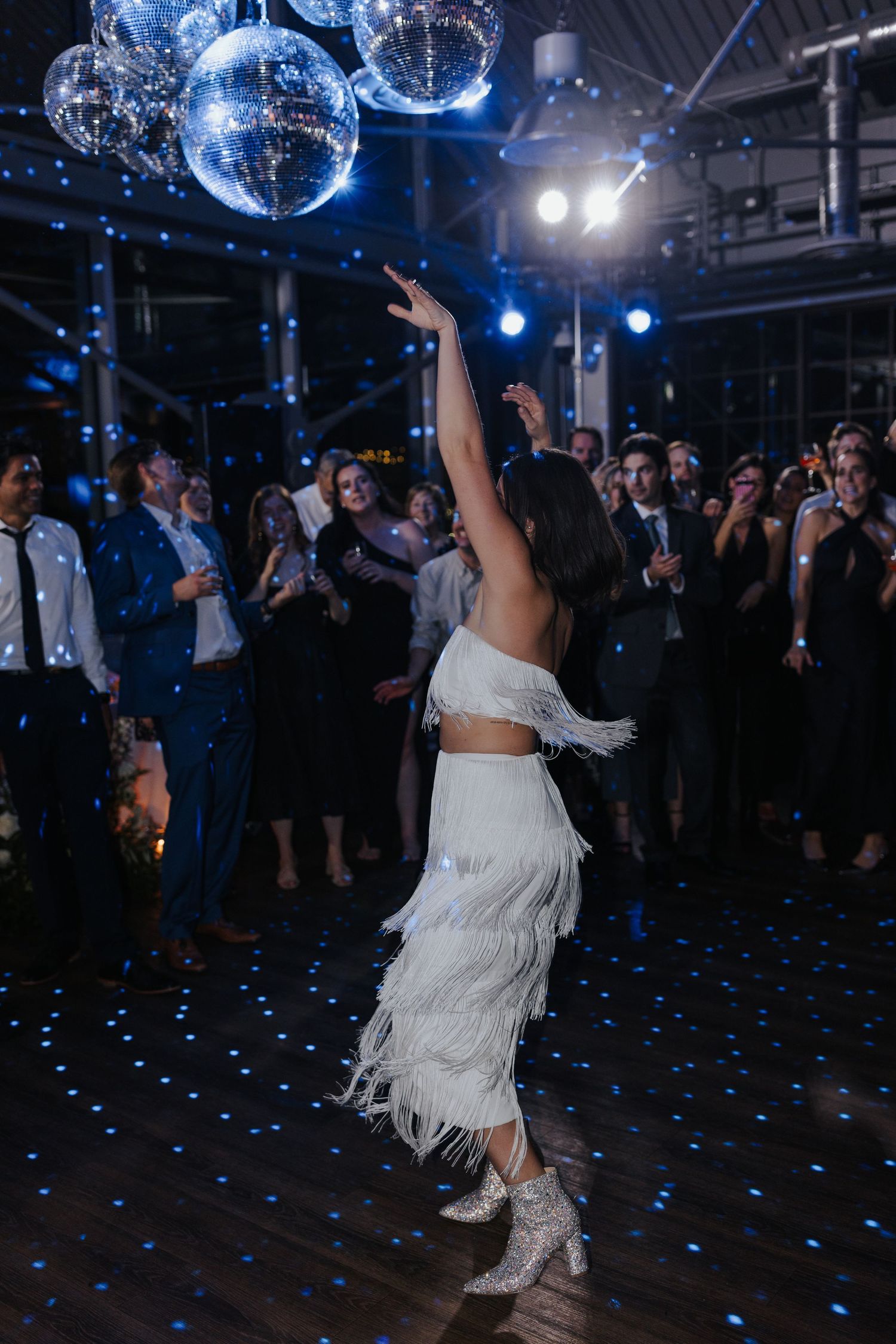 Person in white fringe dress dancing under blue disco ball lighting.