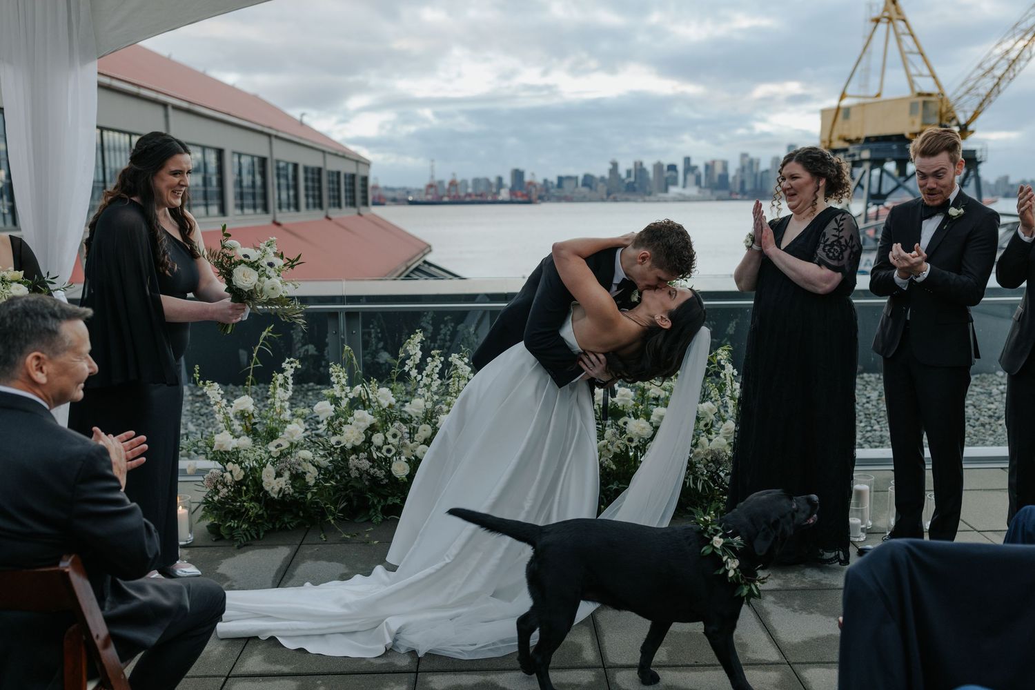 Outdoor wedding ceremony setup on a pier with city skyline views and white floral arrangements.