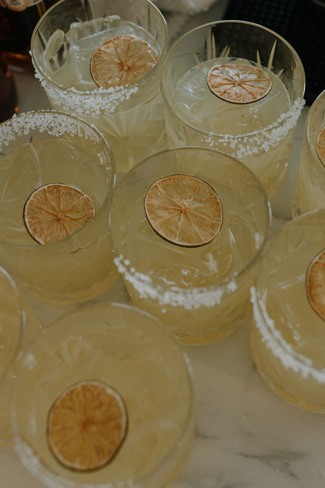Citrus-garnished cocktails with salt rims arranged on marble surface.