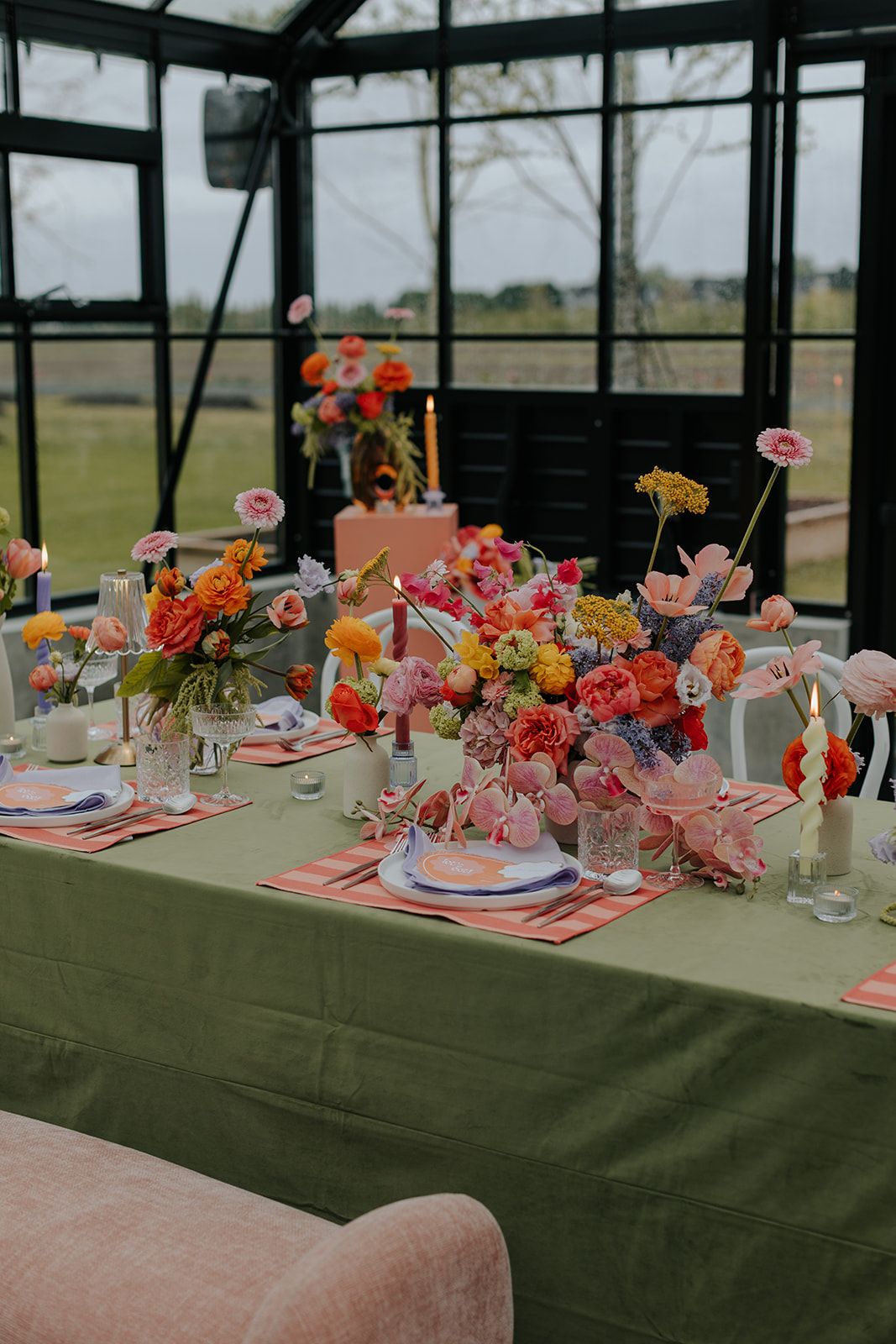 Elegant wedding reception table decorated with pink and coral flowers against a green tablecloth in a glass-walled venue.
