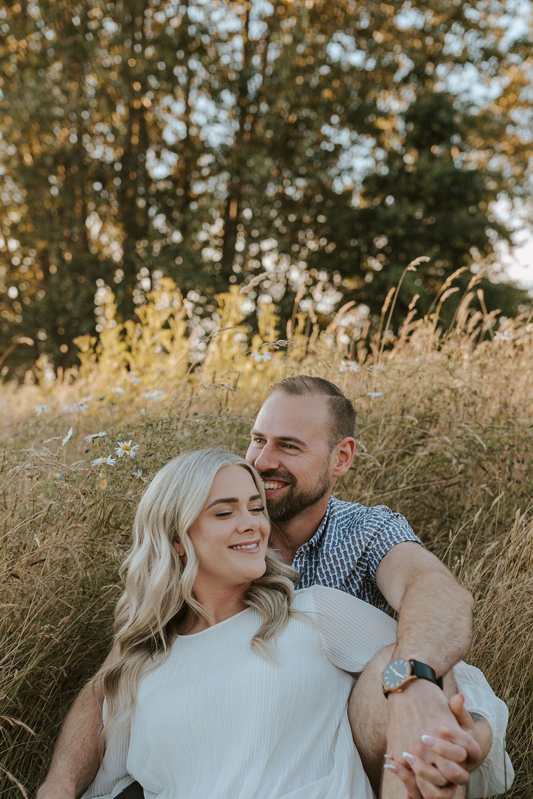A couple relaxes together in a golden field during sunset, sharing tender moments.