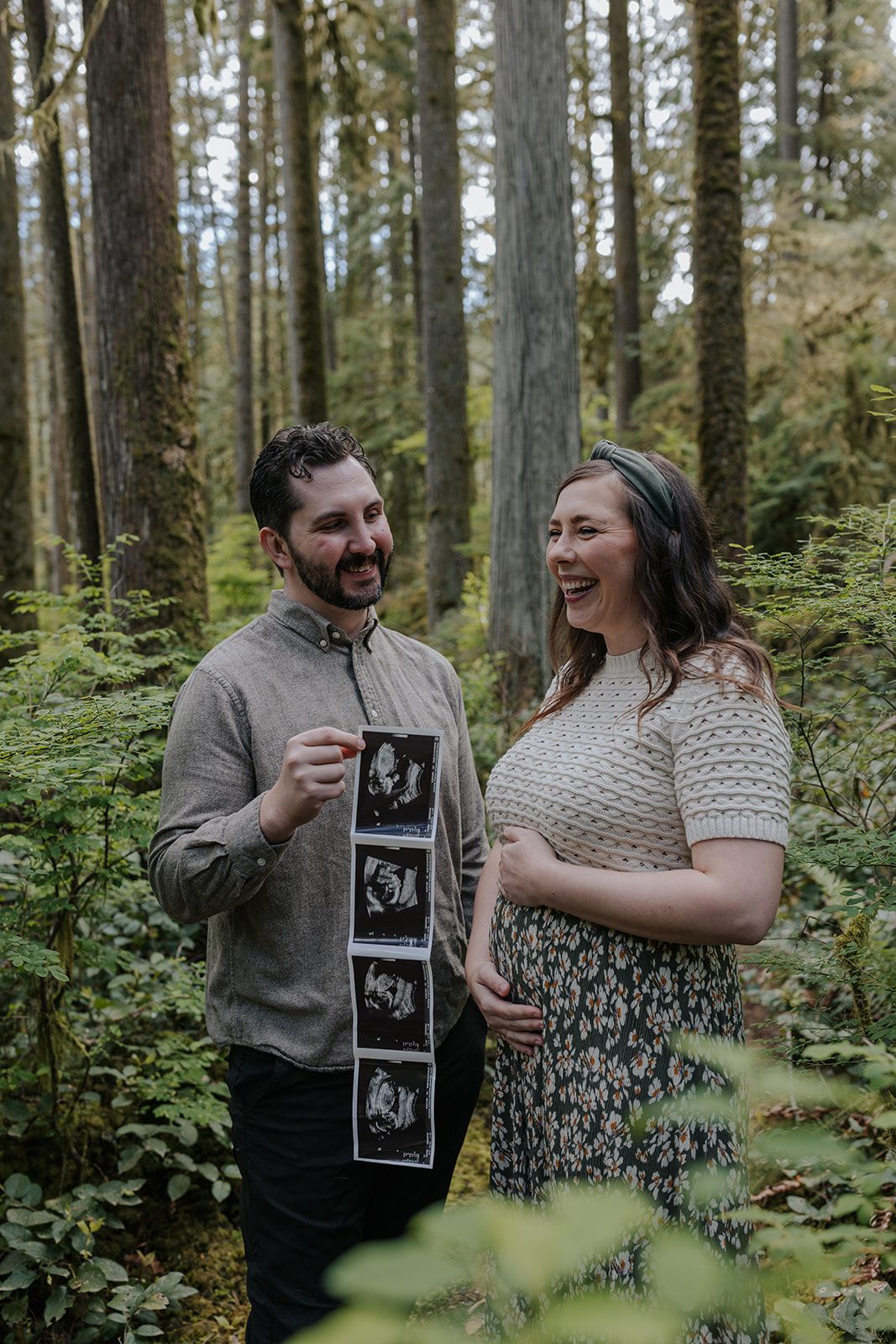 Couple sharing a joyful moment in the forest while holding ultrasound photos.