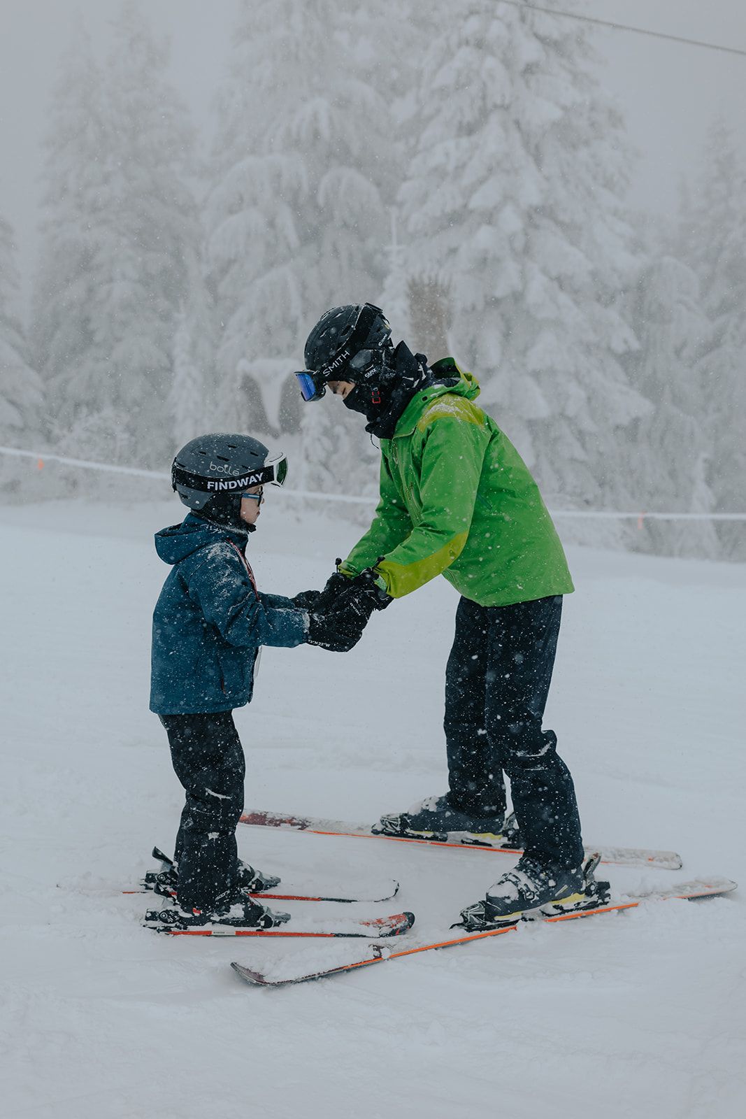 A ski instructor helps a young student learn proper skiing technique in snowy conditions.