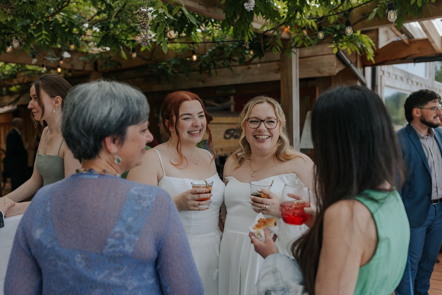 Wedding guests in formal attire enjoying drinks and conversation under a covered patio.