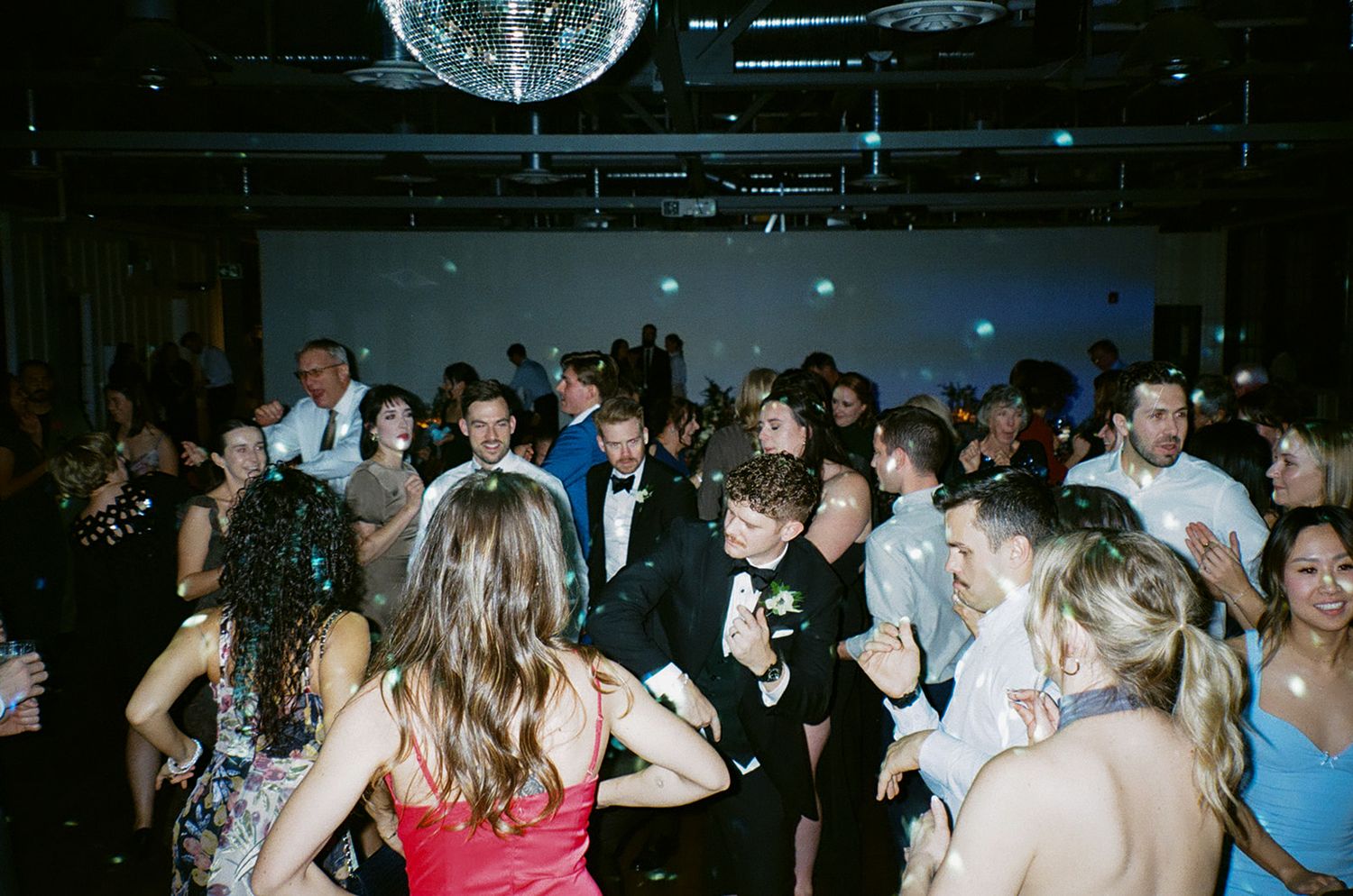 Wedding reception dance floor filled with guests under blue lighting.
