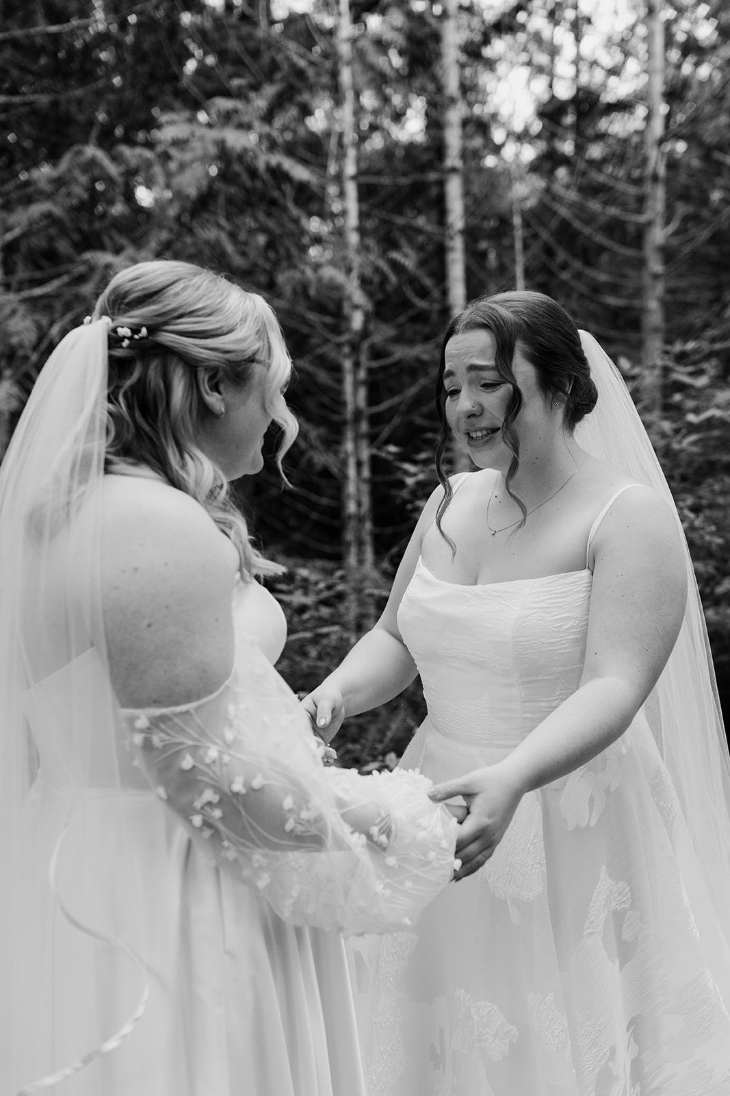 Two people in white wedding dresses dance and laugh together in a forest setting.