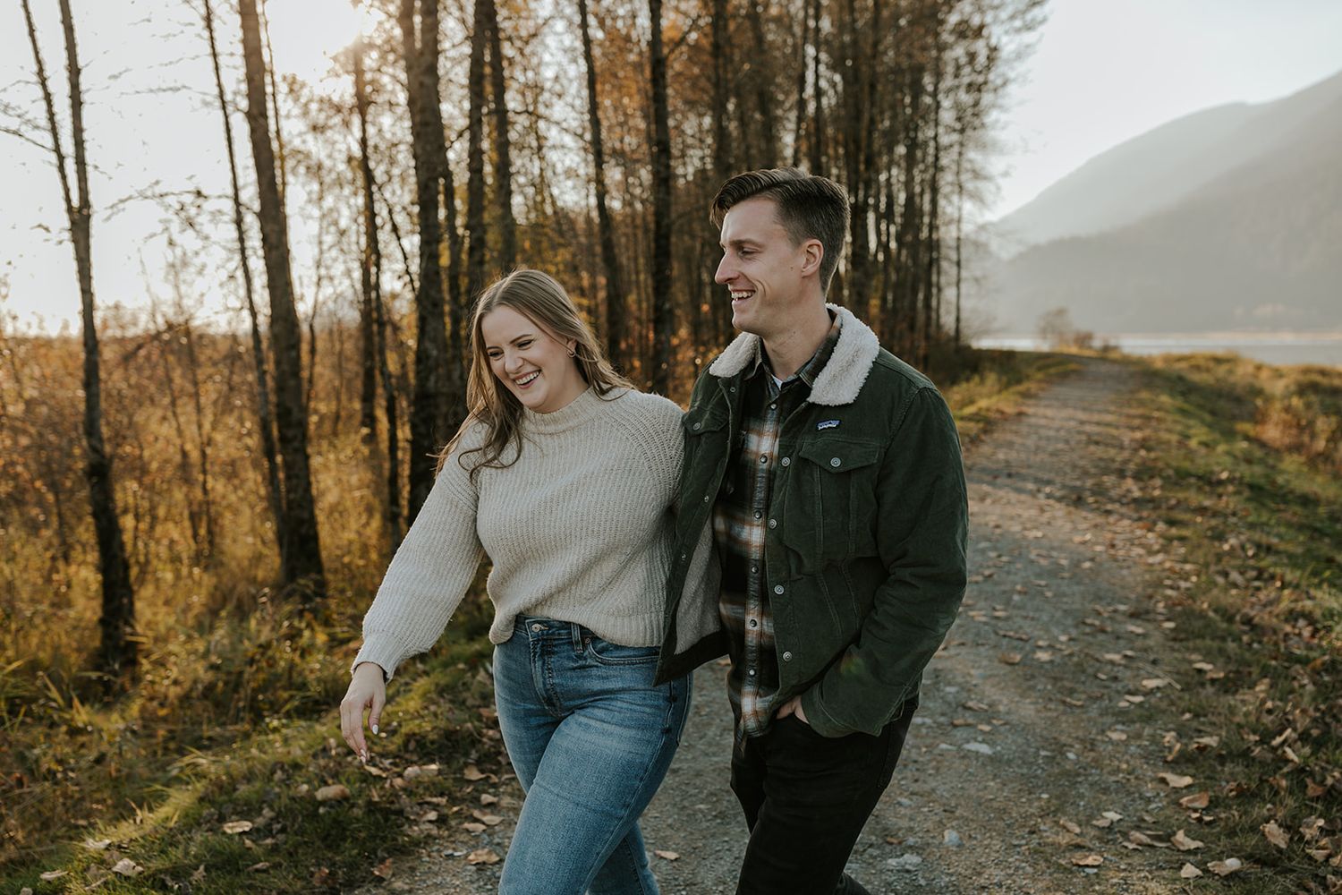 A couple walks together on an autumn trail with golden sunlight filtering through trees.